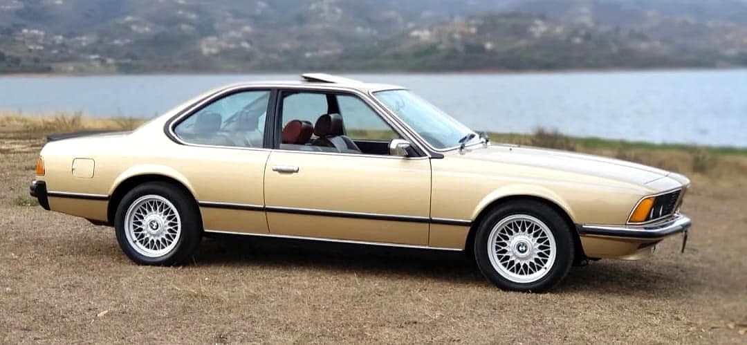 Gold BMW 6 Series E24 coupé with cross-spoke alloys, parked by a lake